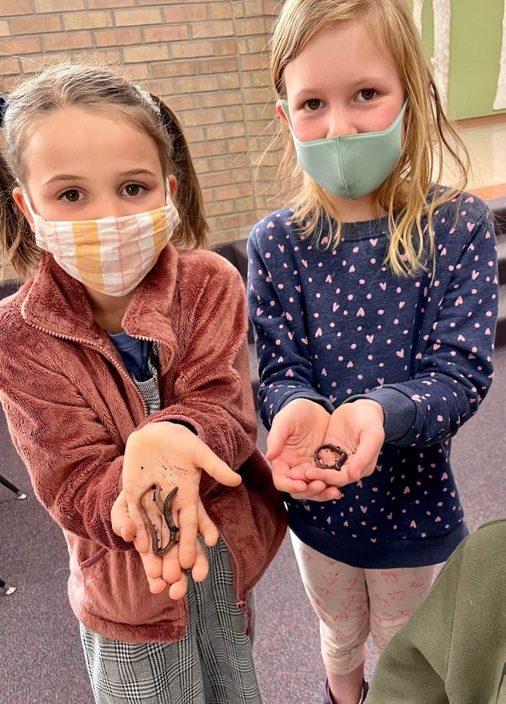 two students holding earthworms outside