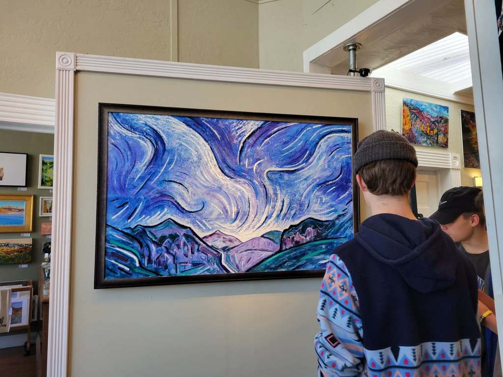 student in art gallery looking at blue lined landscape painting