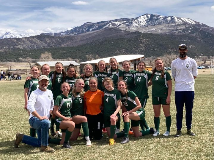 girls soccer team on field together for picture with mountain range in the background